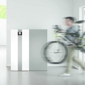 In einem minimalistischen Raum bewegt sich ein Mann schnell mit einem Fahrrad, während ein Kühlschrank im Hintergrund steht.